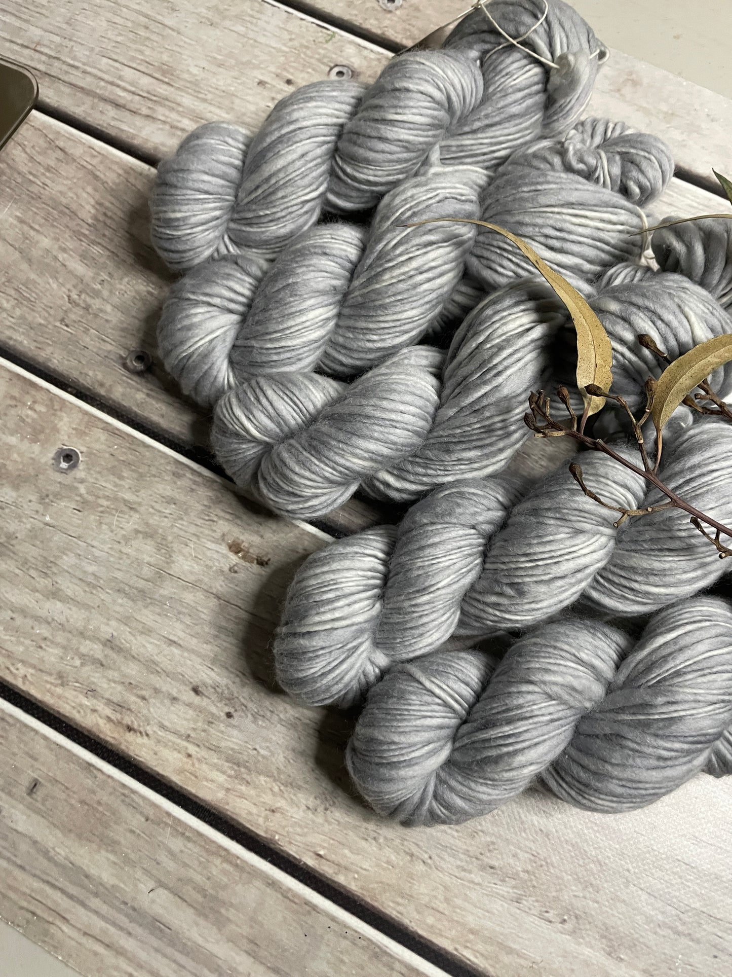 pale silver grey skeins of yarn sit on a wooden floor