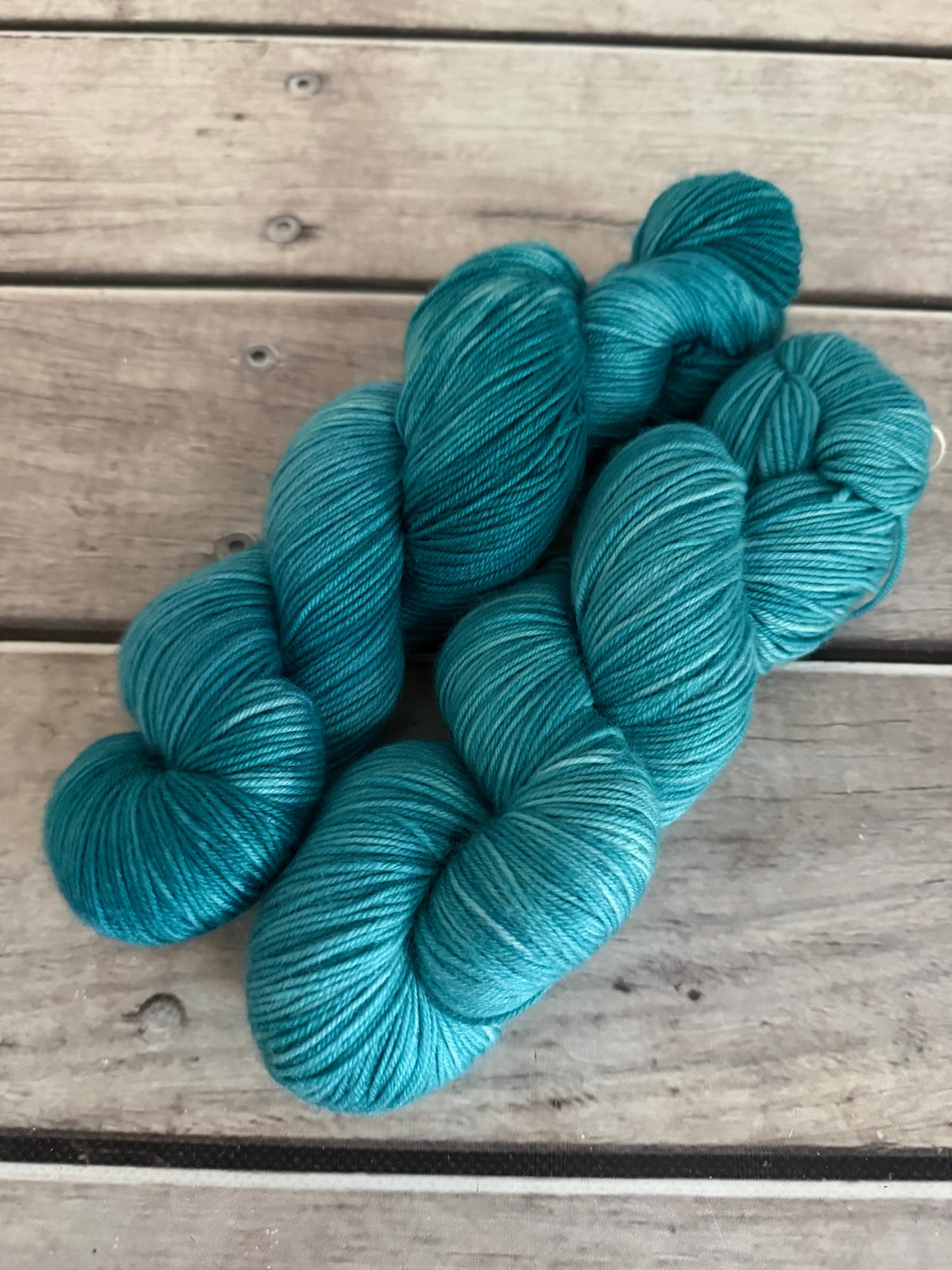 Two skeins of turquoise blue yarn arranged on a rustic wooden plank surface.