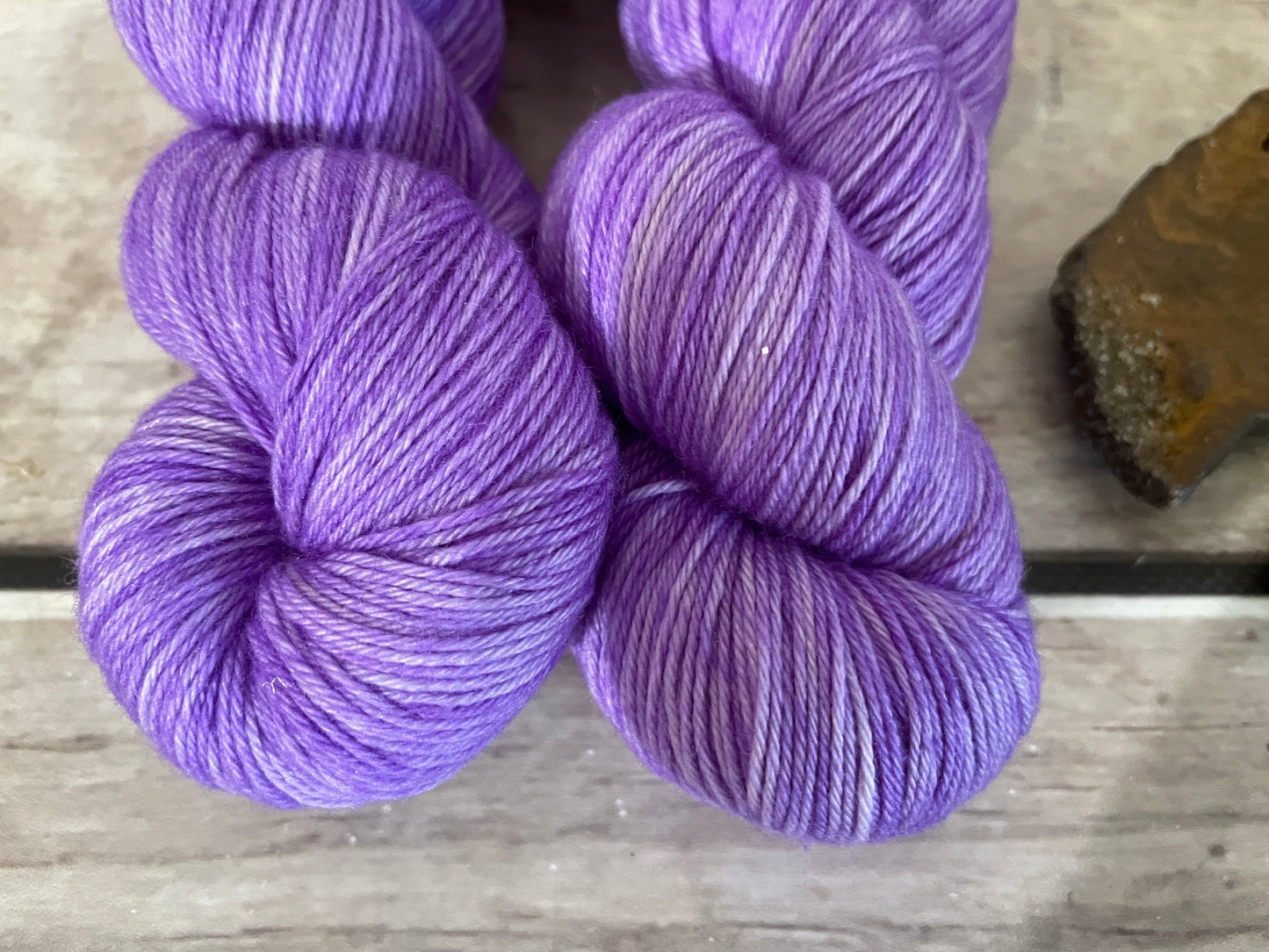 Two flourescent purple skeins of yarn are sitting on a wooden board