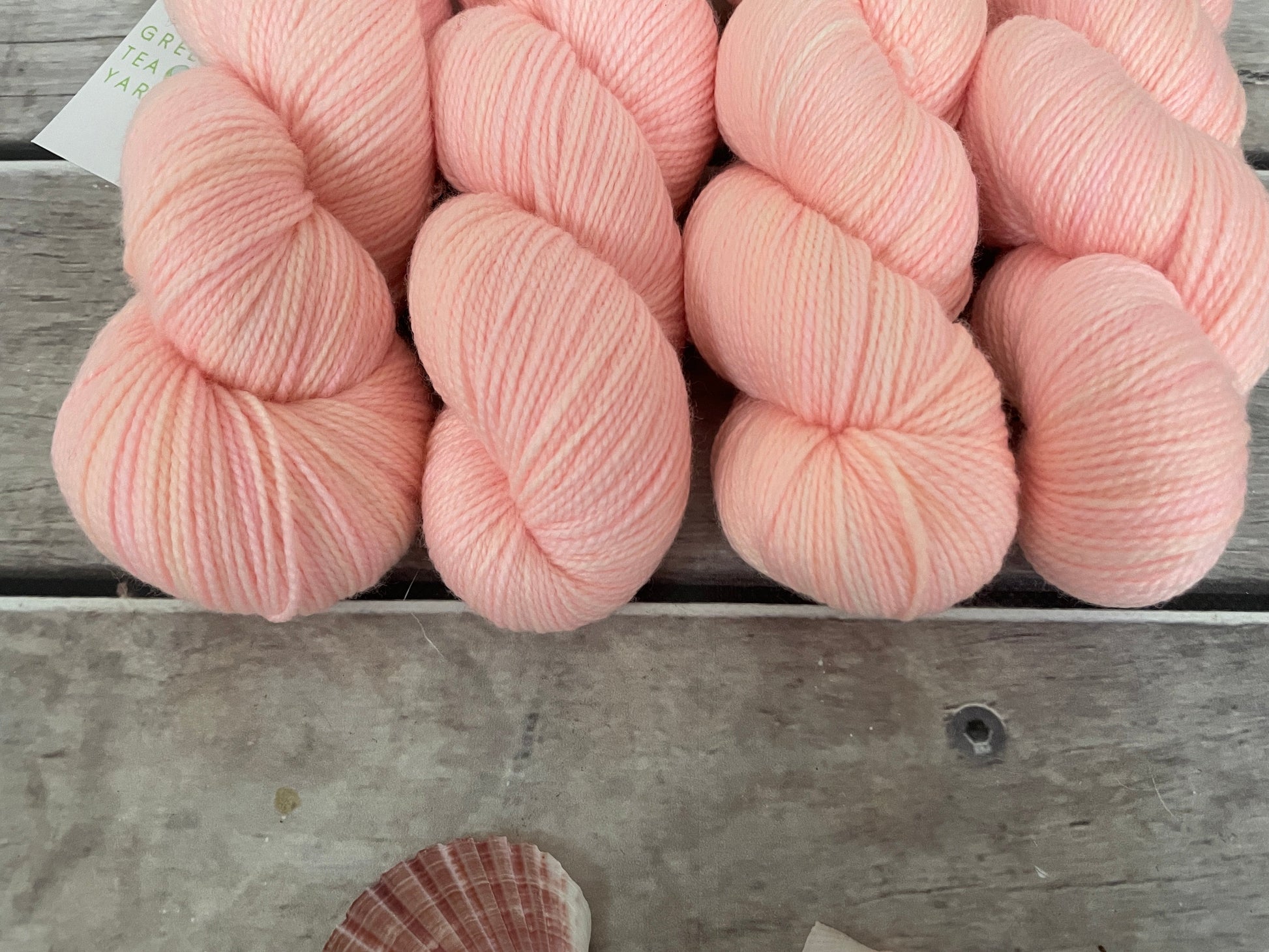A soft pastel peach colour yarn sits on some wooden planks
